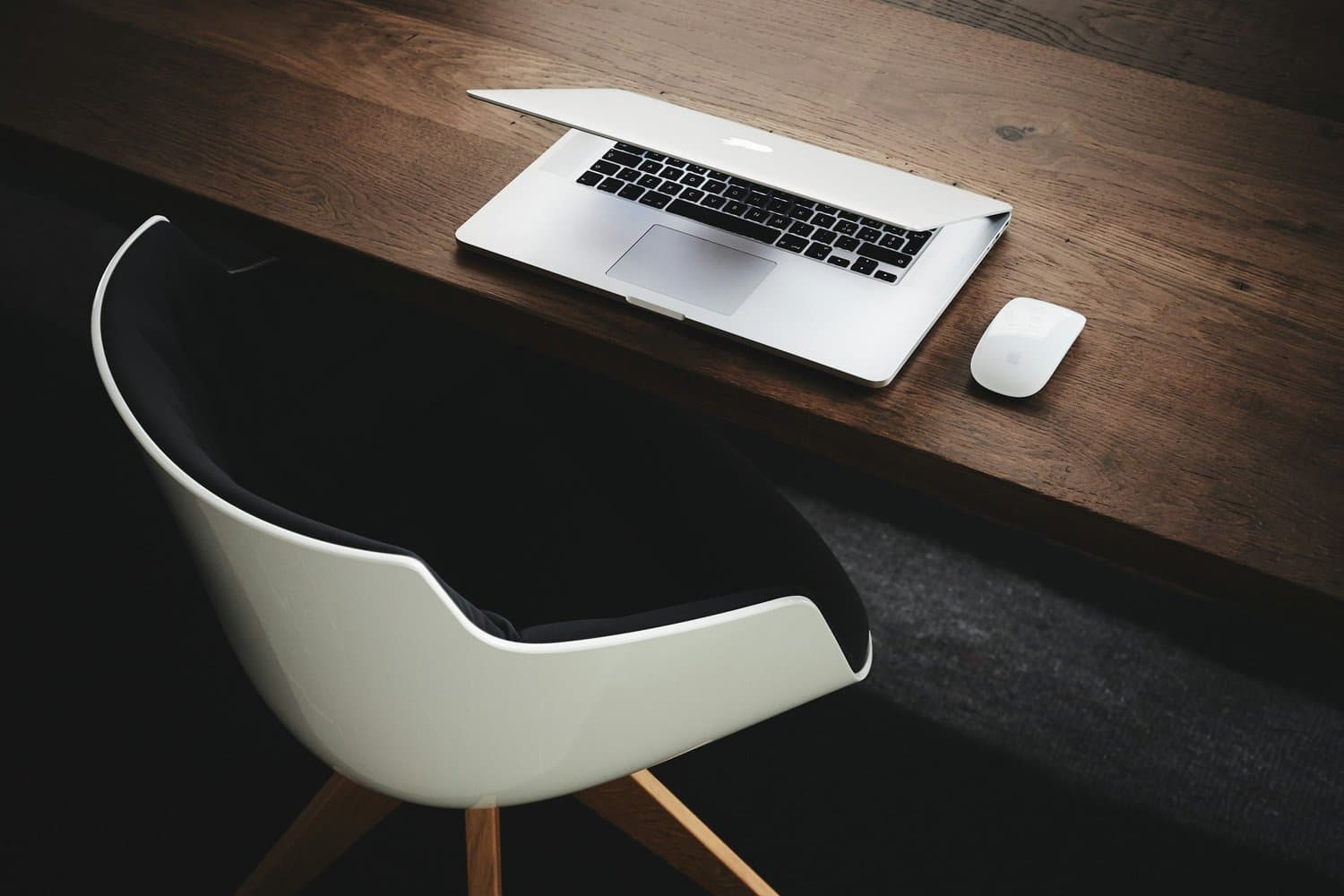 A modern workspace with a wooden desk, a laptop, a wireless mouse, and a stylish chair.